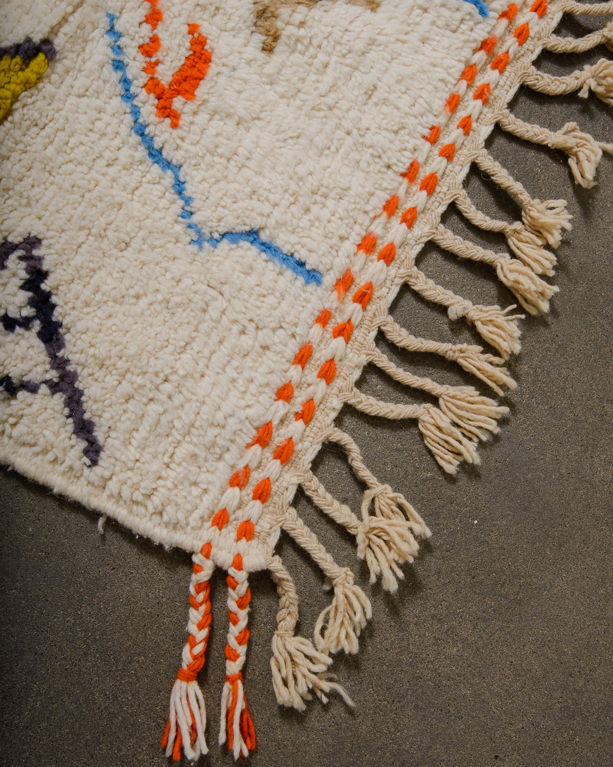 Corner of wool berber rug that is finished with tightly woven ends and natural wool tassels across the ends.