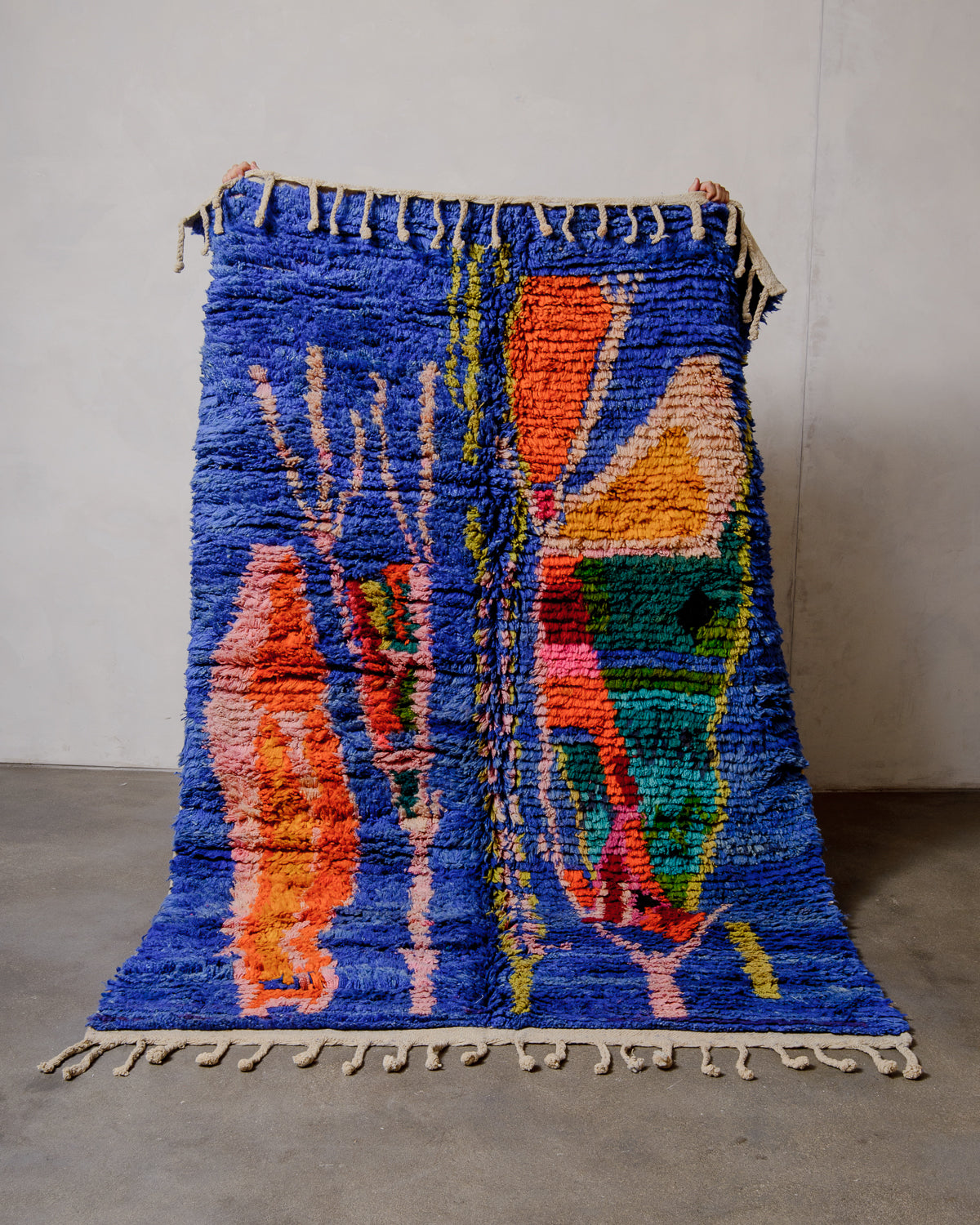 Berberlin vintage boujad rug in colourful wool being held up in front of a white wall.