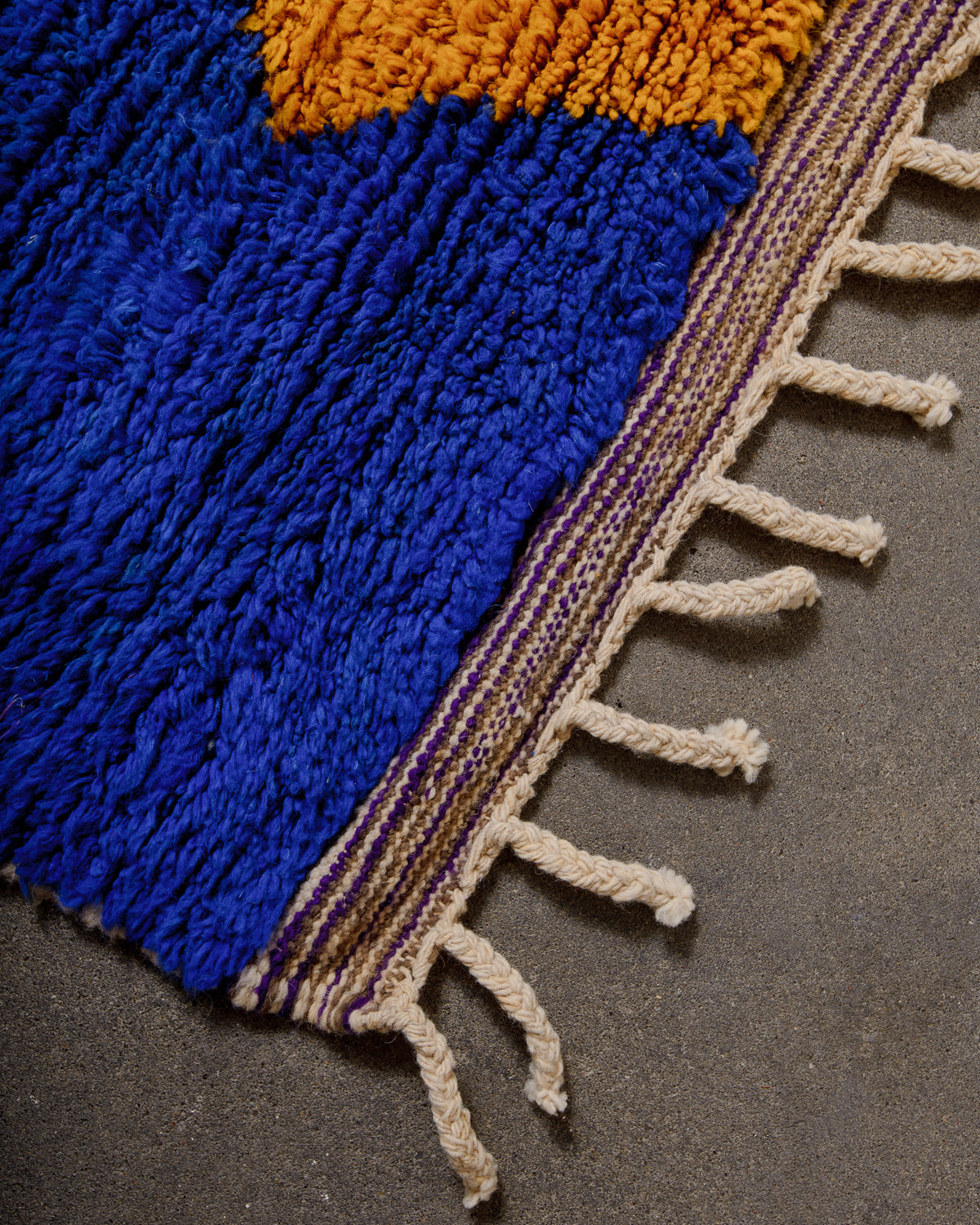 Corner of boujad rug showing woven finish and natural wool tassels at end of rug. 