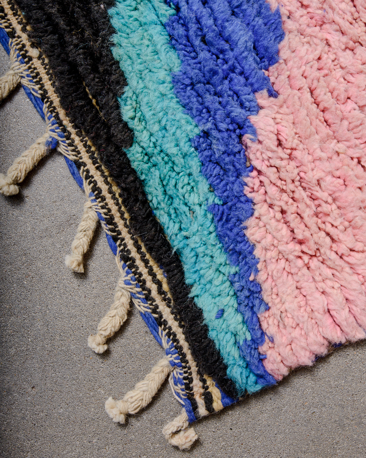 Corner of Berber runner rug with colourful wool pile and natural wool tassels. 