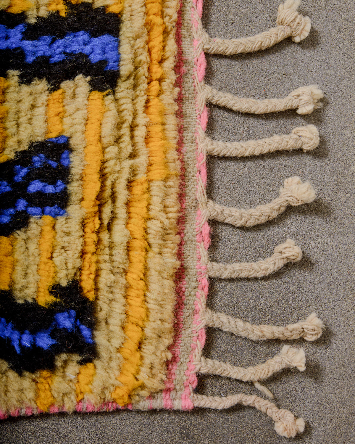 Corner of Berber runner rug with colourful wool pile and natural wool tassels. 