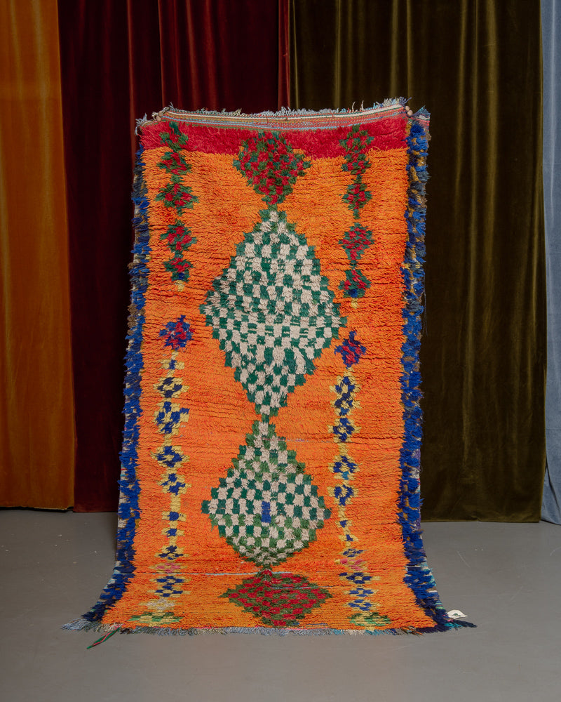 Vintage Berberlin boucherouite runner rug being held up in front of a velvet curtain. 