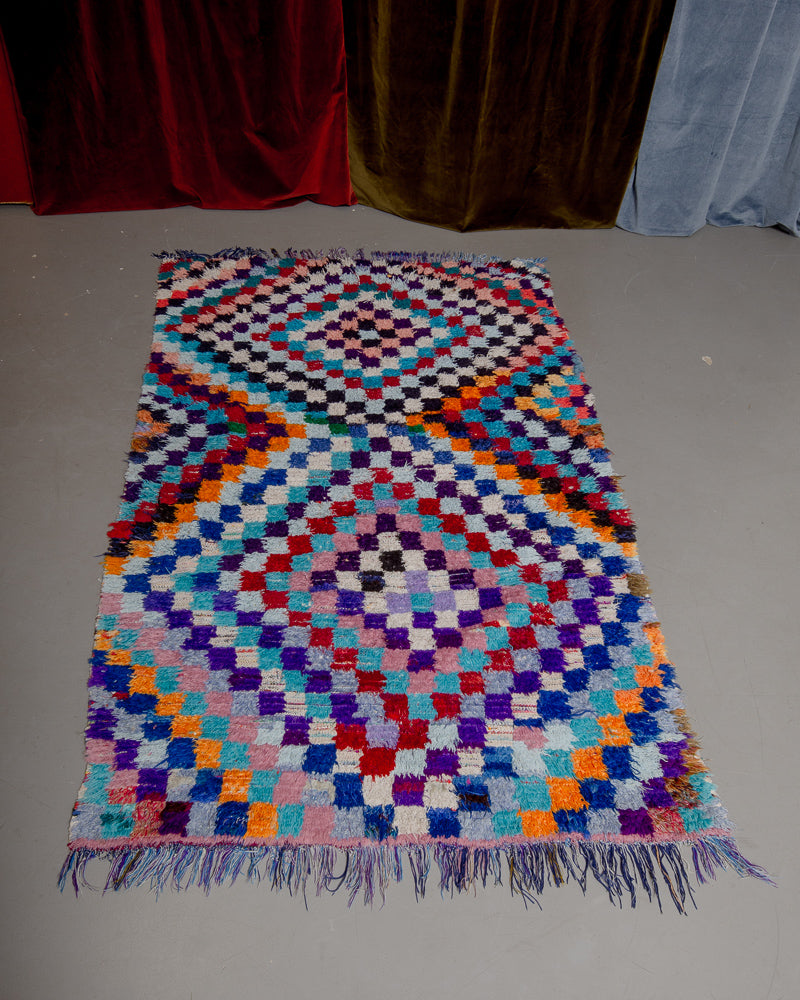 small boucherouite rug featuring purple, orange, blue and red on grey floor. 