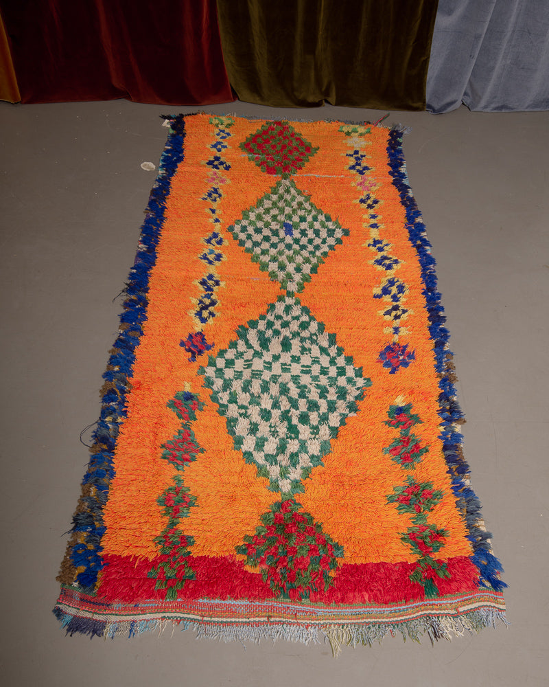 Vintage Berberlin boucherouite runner rug on grey floor in front of velvet curtain. 