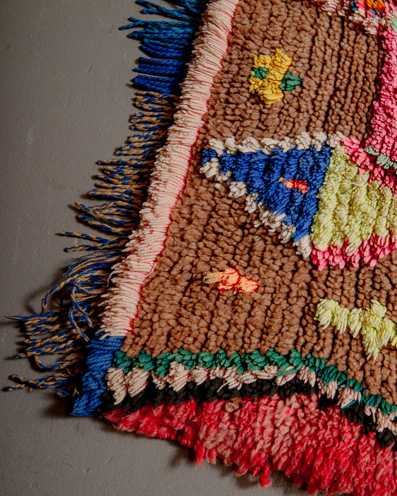 Corner of boucherouite rug with blue, yellow, green and pink cotton and brown and red wool.
