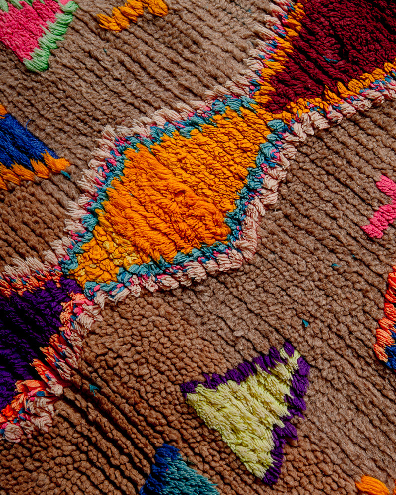 Surface of boucherouite rug with orange, yellow, purple, burgundy and pink cotton and brown wool.