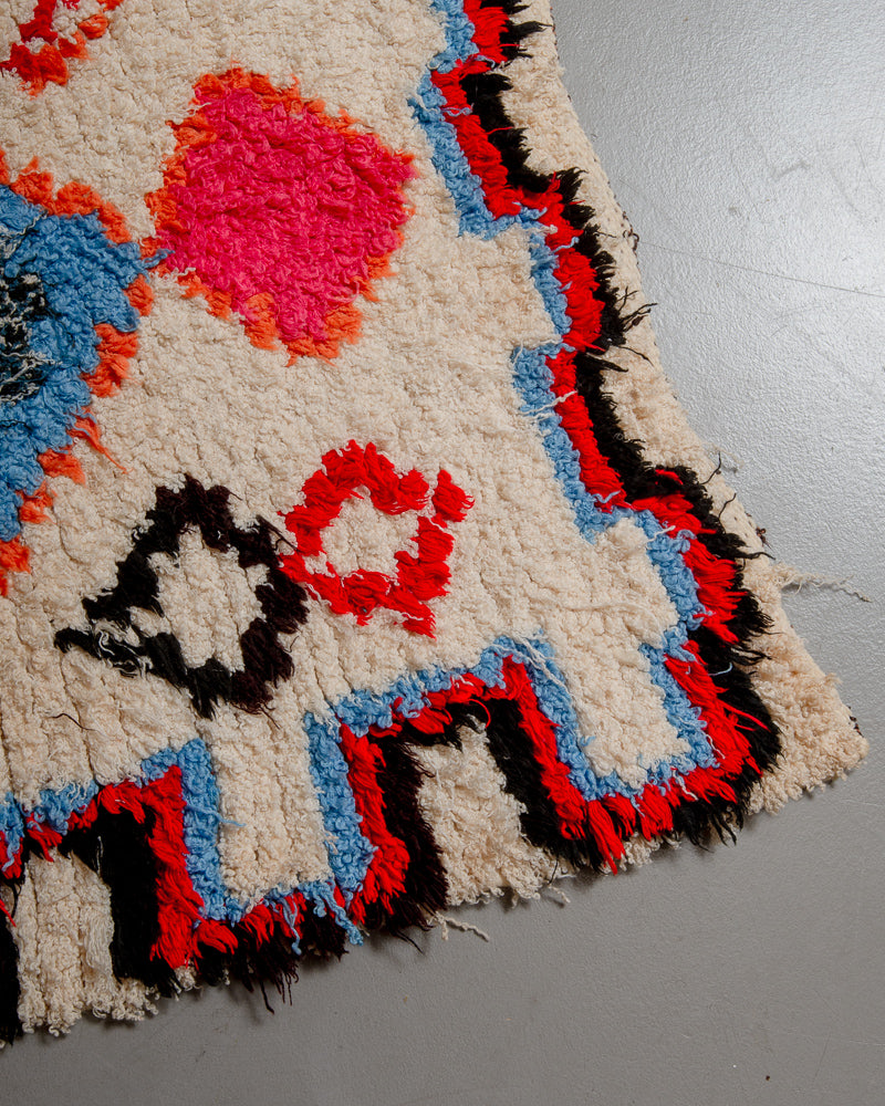 Corner of boucherouite rug with blue, red, orange, black and cream.