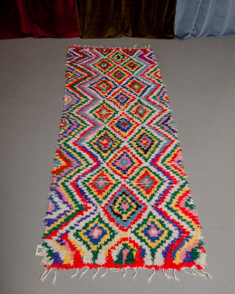 Vintage Berberlin boucherouite runner rug on grey floor in front of velvet curtain. 