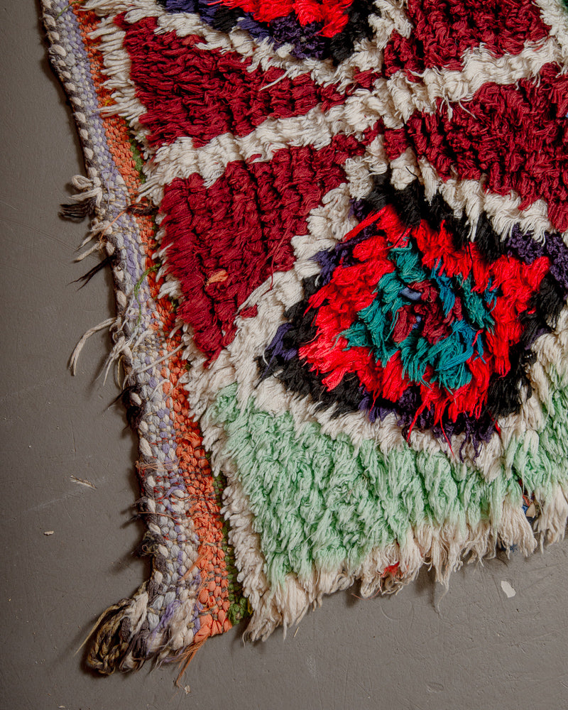 Corner of boucherouite rug with mint, burgundy, red, black and white yarn.
