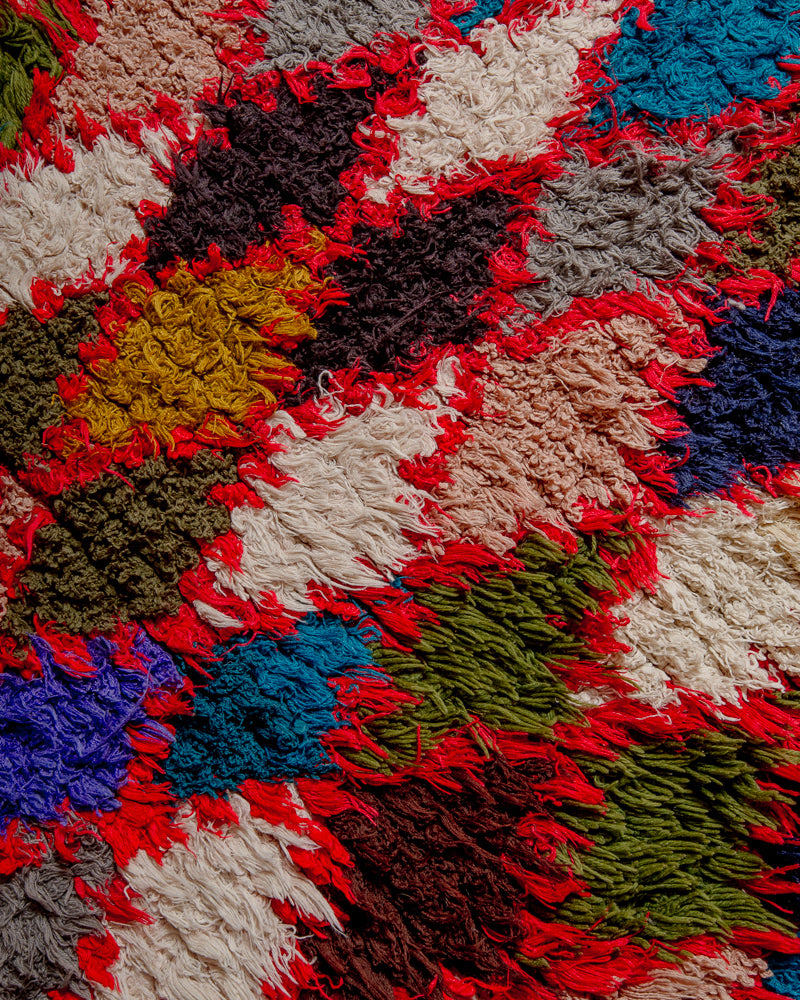 Surface of vintage rug made of recycled cotton and wool, featuring strong red diamond pattern with blue, white, olive and grey.