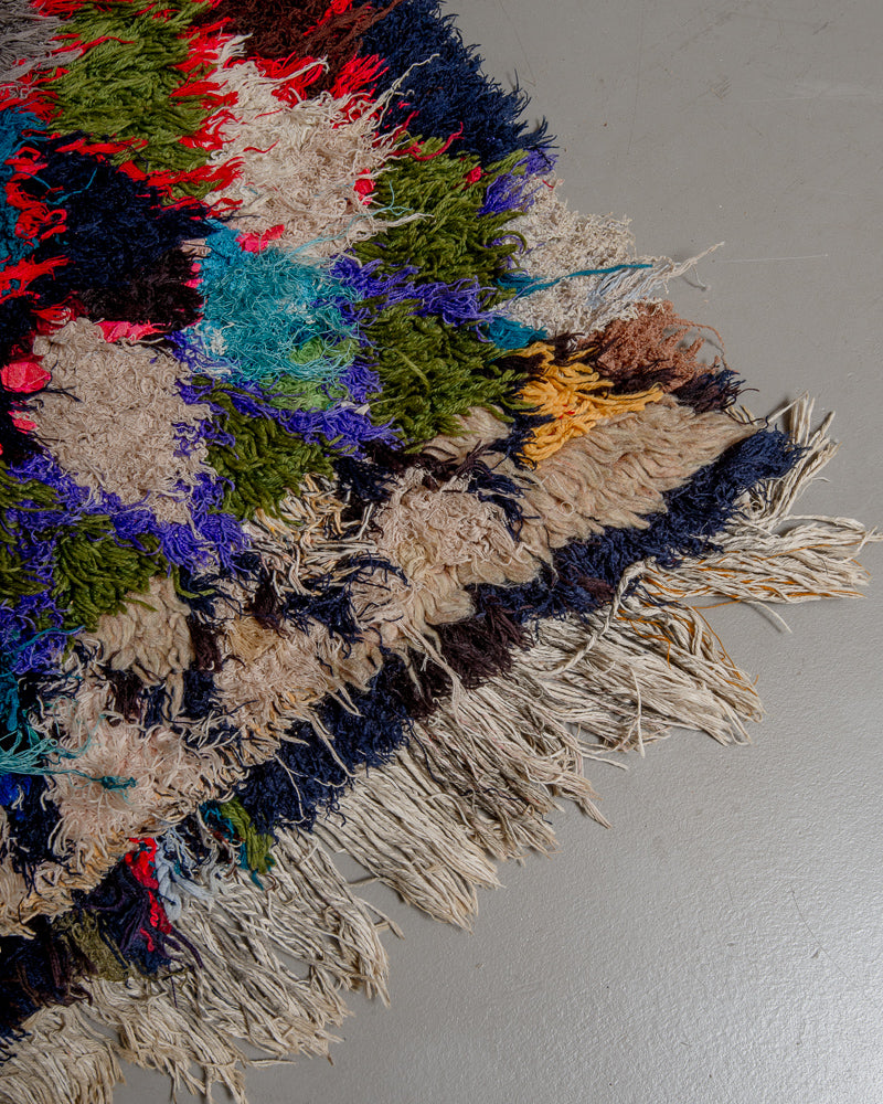 Corner of vintage rug made of recycled cotton and wool, with irregular tassels on a grey floor. 