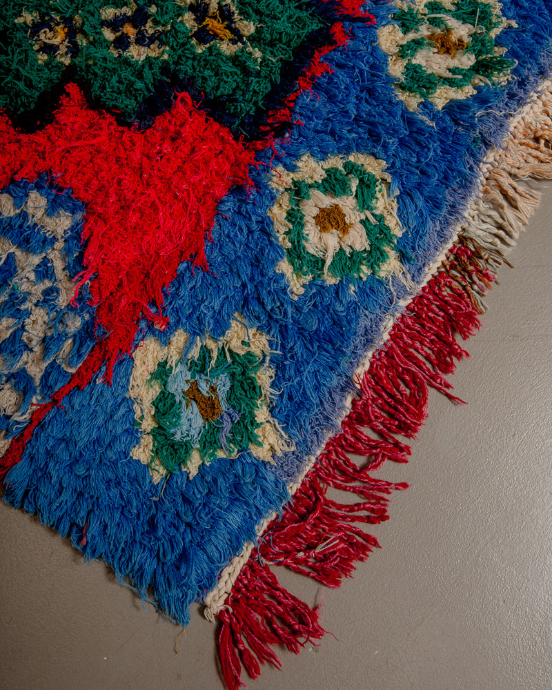 Corner of boucherouite rug with red, blue green and yellow yarn and tassels.
