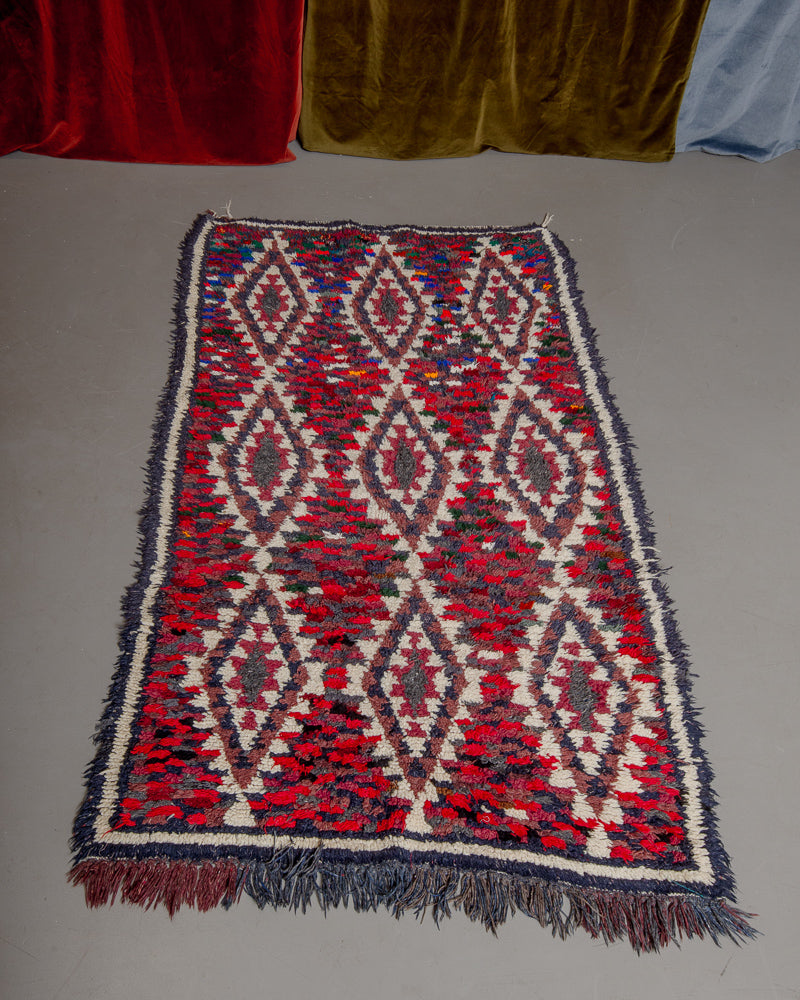 Vintage Berberlin boucherouite runner rug on grey floor in front of velvet curtain. 