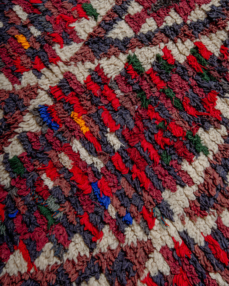 Surface of boucherouite rug with red, blue, grey and brown yarn and cream wool.