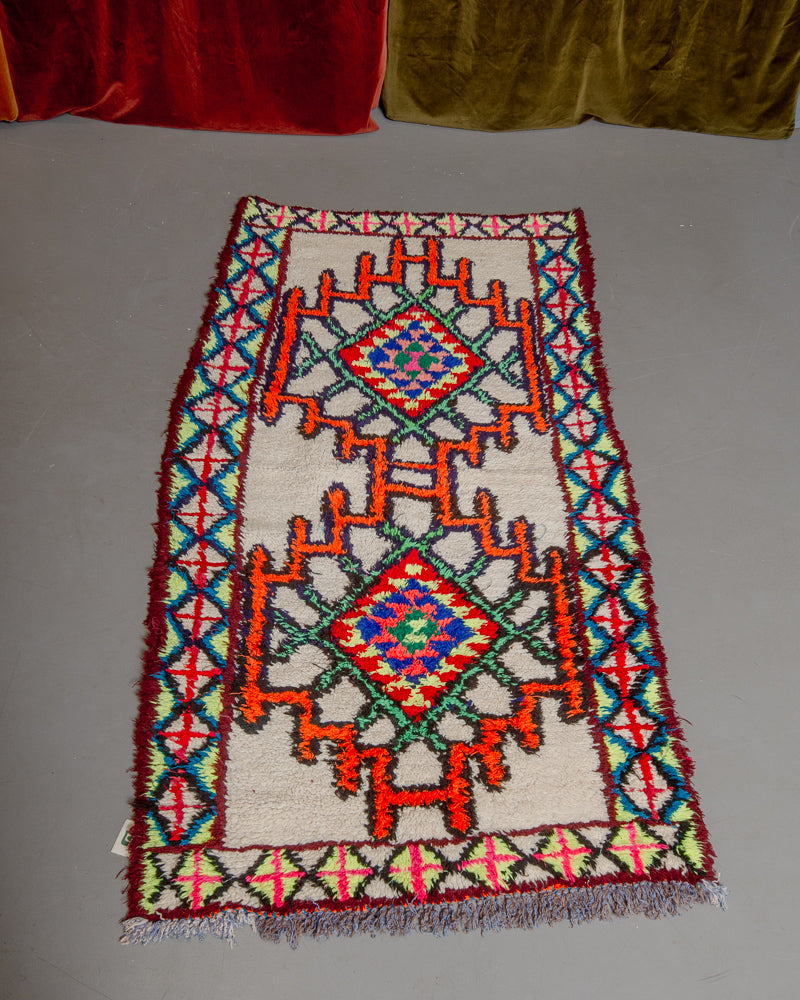 Vintage Berberlin boucherouite runner rug on grey floor in front of velvet curtain. 