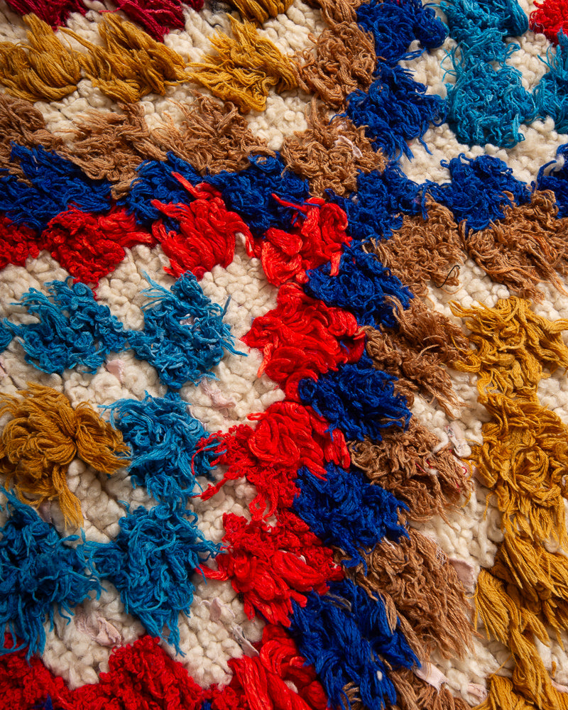 Surface of boucherouite rug with red, blue mustard and brown yarn and cream wool.