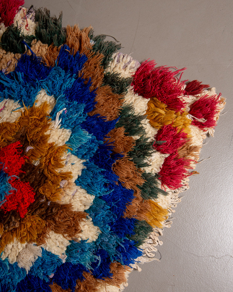 Corner of boucherouite rug with red, blue and brown yarn and cream wool..