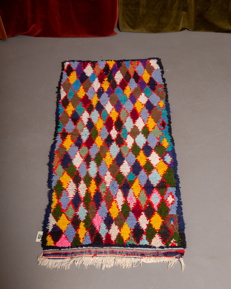 Vintage Berberlin boucherouite runner rug on grey floor in front of velvet curtain. 